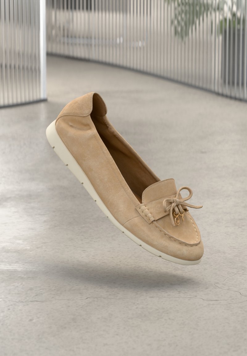 Mocassins en daim beige avec un bout rond, un nœud décoratif et un logo en métal doré, dotés d'une semelle en caoutchouc crème et de détails cousus.