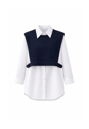 Chemise blanche à manches longues avec une surcouche sans manches bleu marine dotée de sangles latérales boutonnées, présentée sur un fond blanc.