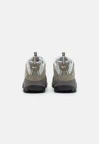 Adidași Nike cu un superior gri și accente verzi, talpă texturată neagră și bucle distincte. Vedere din spate care evidențiază logo-ul și detaliile de cusătură.