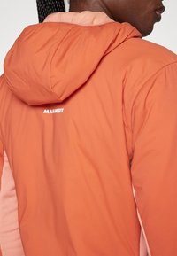 Orange padded jacket with a hood, featuring a lighter pink accent along the side; includes a white logo at the back. Soft texture, casual design.