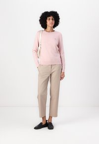 Světle růžový svetr, kulatý výstřih, dlouhé rukávy a malé logo. Béžové rovné kalhoty. Černé boty na slip-on. Minimalistická krémová taška.
