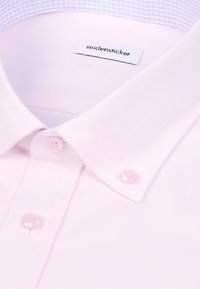 Col de chemise texturé rose clair avec des boutons assortis et une étiquette blanche portant l'inscription "seidensticker" à l'intérieur de l'encolure.