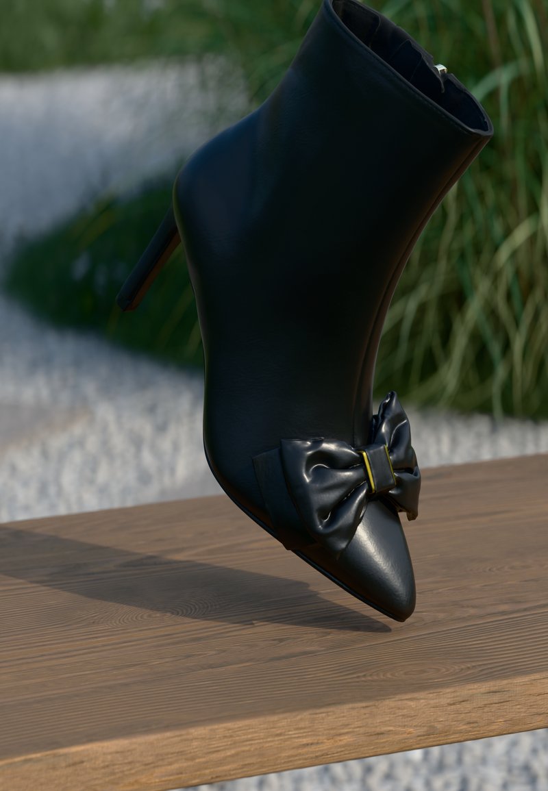 Zwarte leren enkelboot met puntige neus, hoge stilettohak en een opvallende zwarte strik met gele accenten aan de voorkant, geplaatst op een houten oppervlak.