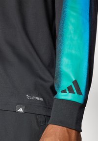 Črna majica z dolgimi rokavi, ki ima rokave v teal gradientu, logo tehnologije ClimaCool in črn Adidasov logo na manšeti. Mehka tkanina.