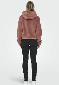 Rosa Kunstfell-Hoodie mit Kapuze, geripptem Saum und langen Ärmeln; kombiniert mit schmalen schwarzen Jeans und cremefarbenen Schuhen. Rückansicht.