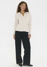 Beige long-sleeve pullover with a collar, paired with loose-fitting black trousers. The fabric appears soft with a smooth texture.