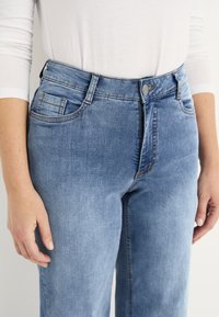 Ljusblå jeans i denim med midjahöjd, fem fickor och sömsatt detaljer. Tyget har en slät struktur och en klassisk passform.