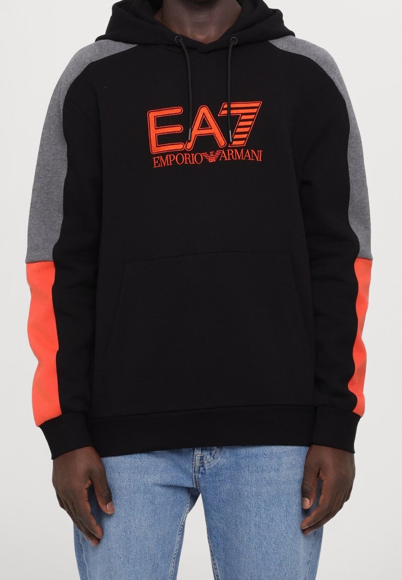 Sudadera negra con acentos en gris y naranja. Presenta el logo de EA7 en naranja, capucha con cordón y bolsillo tipo canguro. Tela suave, corte casual.