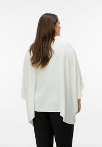 Biała, teksturowana tunika o luźnym, oversize’owym kroju i szerokich rękawach, noszona na czarnych spodniach, widziana od tyłu.