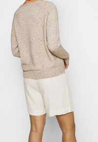 Pull en tricot beige avec ourlet et poignets côtelés, associé à un short en lin beige clair présentant une texture légèrement froissée.