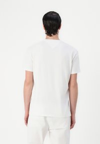 White cotton t-shirt with short sleeves, round neck, and a plain design. Features a seamless back with a subtle v-shaped yoke.