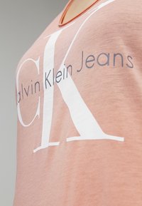 T-shirt av bomull i ljusrosa med rundad halsringning och stort vitt "CK"-logotyp. Mjukt tyg med subtil textur och tryckt varumärke.