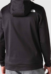 Hoodie noir en tissu doux, doté d'une capuche, de manches longues et d'un accent logo près de l'épaule. Texture lisse, design ajusté.