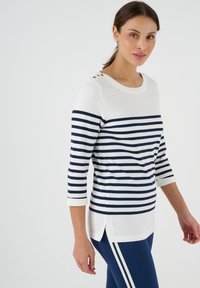 Gestreiftes Oberteil in Weiß und Navy mit drei Viertel-Ärmeln, runder Halslinie und seitlichen Schlitzen; hat dekorative Knopfakzente an den Schultern.