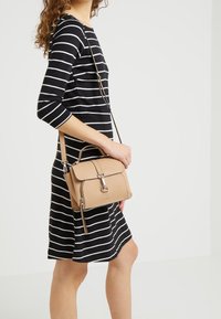 Beige texturovaná kabelka s horním uchopovačem a odnímatelným ramenním popruhem, vybavená zapínáním na klips a jemným logem na přední straně.