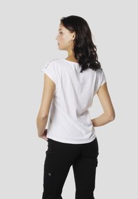 T-shirt blanc à manches courtes et encolure arrondie, avec des détails en dentelle sur les épaules, associé à un pantalon noir.