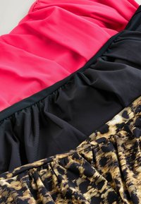 Trzy sekcje materiału: górna w jaskrawym różu, środkowa w jednolitym czarnym, a dolna w czarno-złotym wzorze zwierzęcym, z falbaniastymi wzorami na całej powierzchni.