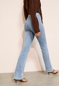 Blugi evazați din denim albastru deschis, cu talie medie, având un design clasic cu cinci buzunare și ușoare efecte de uzură. Asortați cu un pulover tricotat maro.