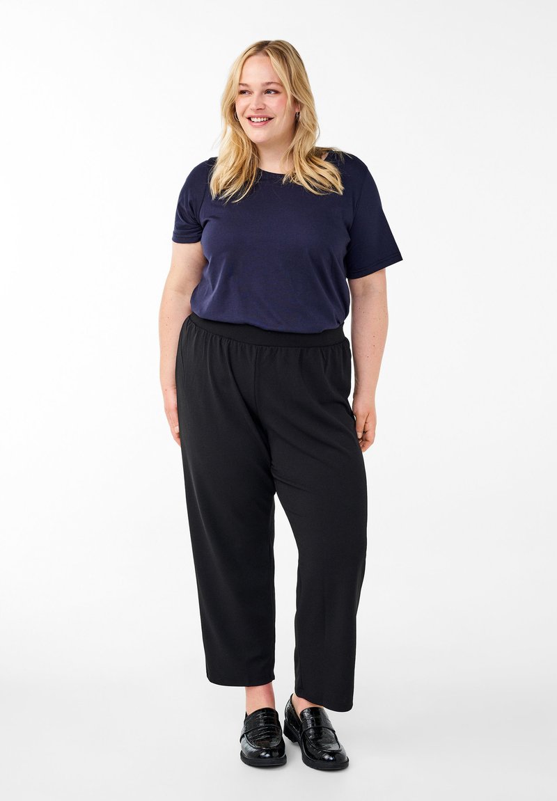 Marineblaues T-Shirt mit kurzen Ärmeln, schwarze elastische Hose und glänzende schwarze Slipper. Einfacher, lockerer Schnitt mit weichem Stoff und knöchellangen Hosen.