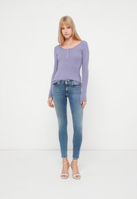 Lilla ribbet langermet topp med sco neckline og knappdetalj, kombinert med blå tettsittende jeans og beige hælsandaler.