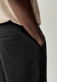Pantaloni neri casual con una texture morbida, vita elastica, tasche laterali e una tasca posteriore caratterizzata da un dettaglio a striscia sottile.