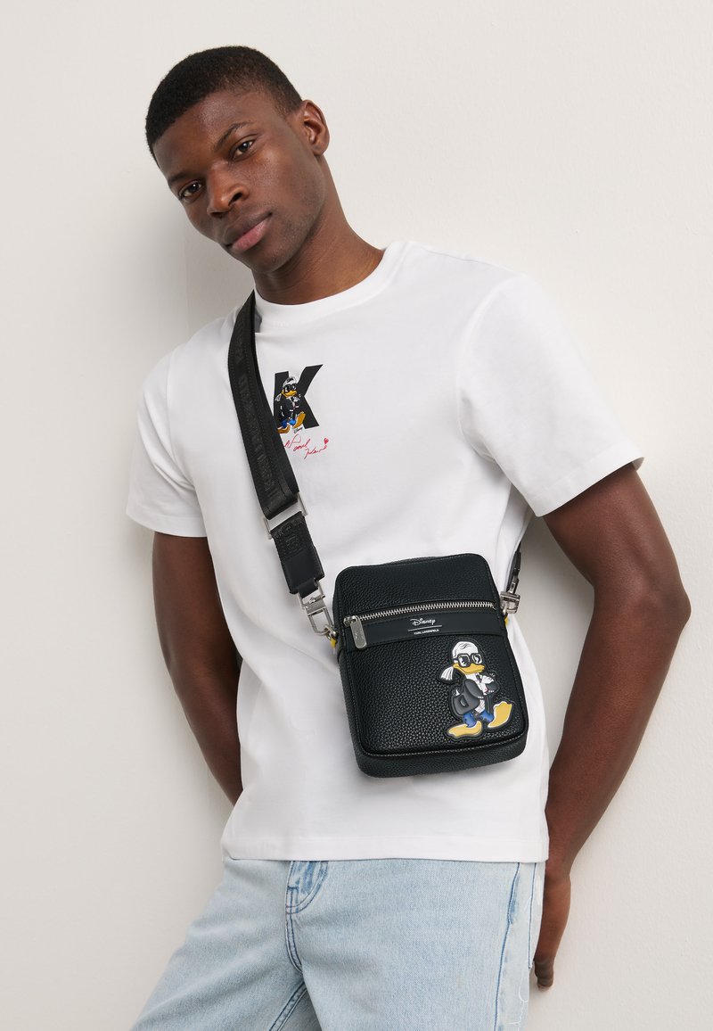 Black leather crossbody bag with textured finish, featuring a zipper, adjustable strap, and a Donald Duck graphic on the front.