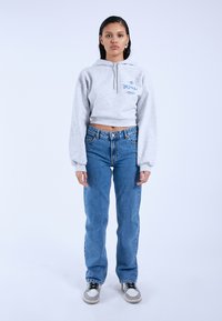 Gray cropped hoodie with a front zipper, featuring blue printed graphics. Paired with light blue denim jeans and gray sneakers.