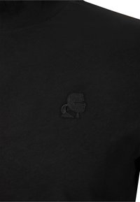 Schwarzer Rollkragenspullover aus Baumwolle, mit einem kleinen, schwarzen gestickten Logo auf der linken Brust, glatter Textur und enganliegendem Design.