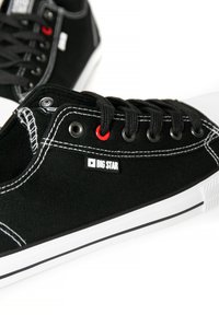 Zapatillas de lona negras con acentos blancos, puntera redonda, cordones negros, ojetes rojos, costuras prominentes y un logo "BIG STAR" en el lateral.