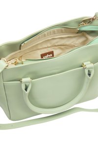 Sac à main en cuir vert clair avec double poignée et bandoulière détachable. L'intérieur comporte des compartiments zippés et un revêtement en tissu beige.