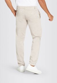 Beige chinos with a slim fit, featuring back pockets with button closures, worn with white sneakers. Smooth texture, casual design.