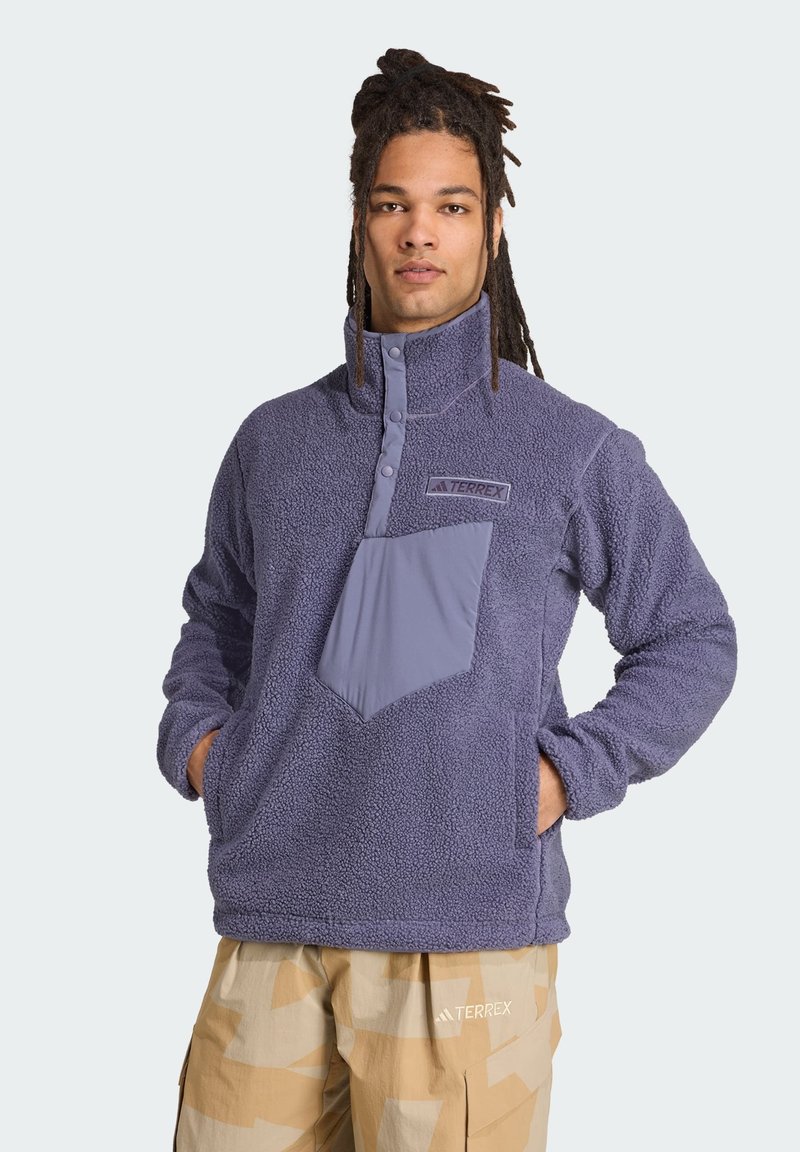 Fleece pullover i blød lilla, med høj krave, delvis knaplukning og en kontrasterende frontlomme. Glat tekstur med logodetalje.