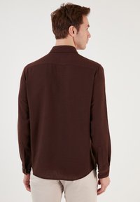 Barna hosszúujjú ing, texturált anyag, puha felület, gombos mandzsetta, laza szabás oldalsó hasítékokkal, hátsó yoke részlettel.