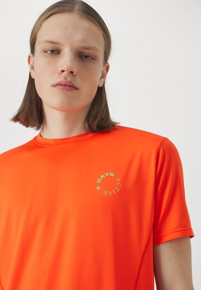 Lys orange atletisk t-shirt med korte ærmer, der har et tekstureret stof og et cirkulært grafisk design i grøn, som står "7 DAYS ACTIVE".