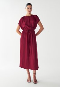 Vestido burdeos de largo medio, hecho de una tela ligera, con escote fruncido y cintura elástica, con mangas cortas y un detalle de cordón.