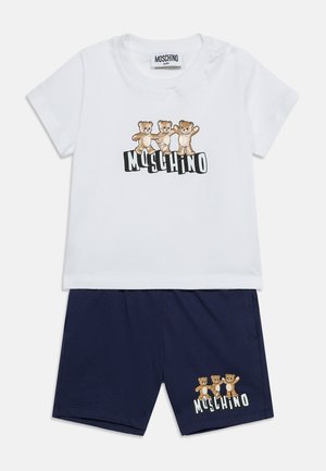 Valge lühikeste varrukatega t-särk ja tumesinised püksid, millel mõlemal on trükitud kolm karu ja sõna "Moschino".