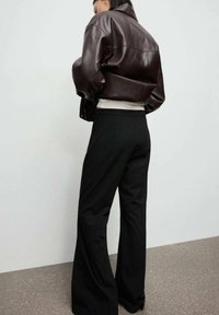 Brązowa skórzana kurtka typu cropped, biała warstwowa bluzka i czarne, wysokie spodnie z szerokimi nogawkami. Gładkie faktury i klasyczne sylwetki.