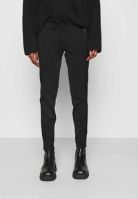 Svarta tapered-byxor tillverkade av ett mjukt material, med dragsko i midjan och sidofickor med dragkedja, tillsammans med svarta ankelstövlar.