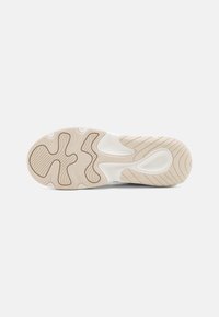 Beige és fehér gumiból készült sneaker talp. Texturált mintázatokkal, barázdákkal és lekerekített formákkal rendelkezik a tapadás és a rugalmasság érdekében.