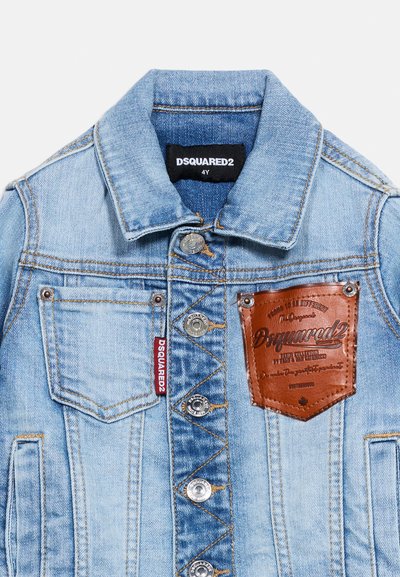 Ανοιχτό μπλε τζιν μπουφάν με ασημένια κουμπιά, δύο τσέπες στο στήθος, ένα καφέ δερμάτινο ταμπελάκι με λογότυπο και μια κόκκινη υφασμάτινη ετικέτα μάρκας.