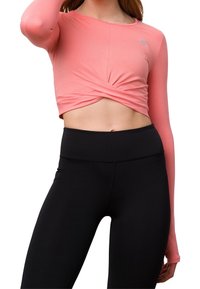 Světle růžový crop top s dlouhým rukávem a designem s překrouceným předkem, doplněný o černé legíny s vysokým pasem vyrobené z hladké, elastické látky.