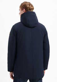 Marineblauwe gewatteerde hoodie met een gladde textuur en verticale naden, zichtbaar vanuit de achterkant.
