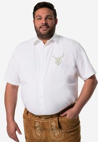 Camicia bianca a maniche corte con ricamo di un cervo sul davanti, abbinata a lederhosen marroni con cuciture decorative sulle tasche.