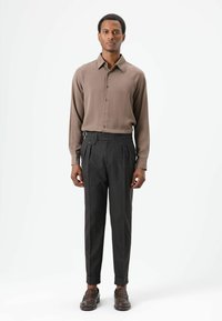 Bruin overhemd met lange mouwen en knopen, gecombineerd met hooggetailleerde, donkergrijze, gestructureerde broeken met een zijspeld. Bruine loafers maken de look af.