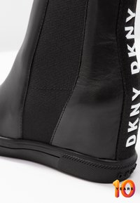 Zwarte enkellaars met een glad leren afwerking en elastische textielen panelen. Heeft witte merkopdruk aan de zijkant en een gerubberde, gestructureerde zool.