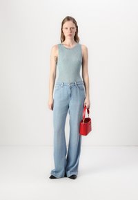 Un débardeur à côtes bleu clair associé à un jean en denim léger à taille haute et coupe ample. Un petit sac à main rouge est tenu dans la main droite.