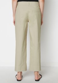 Beige wijde katoenbroek met een achterzak, voorzien van een rechte snit en gezoomde randen, gecombineerd met eenvoudige zwarte sandalen.