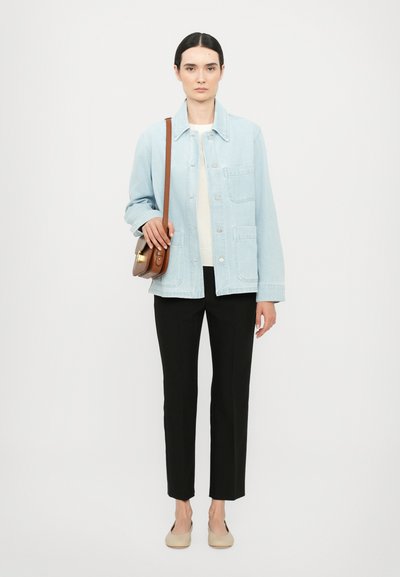 Light blue denim jacket with button closure and patch pockets, paired with a cream top and black straight-leg trousers. Brown crossbody bag and beige flats.