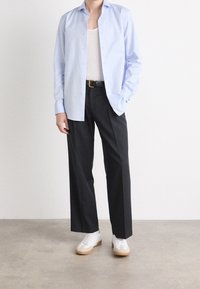 Světle modrá košile na knoflíky s dlouhými rukávy, černé kalhoty s širokými nohavicemi a bílé tenisky s béžovými podrážkami. Neformální a pohodlný střih.