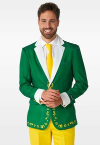 Blazer verde con colletto e polsini bianchi, ricami floreali gialli, abbinato a pantaloni gialli brillanti e una cravatta gialla.
